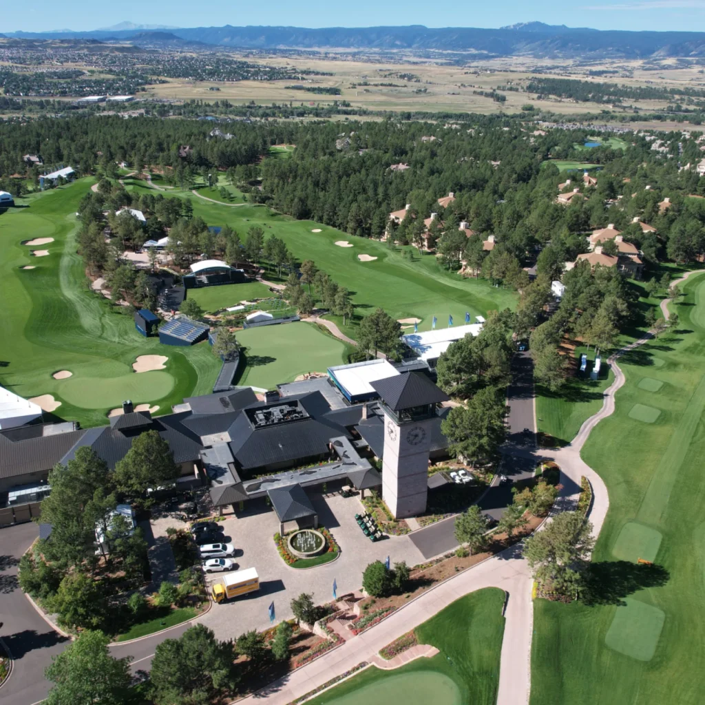 A scenic aerial view of a golf course with lush greens and a clubhouse surrounded by trees in a mountainous region.