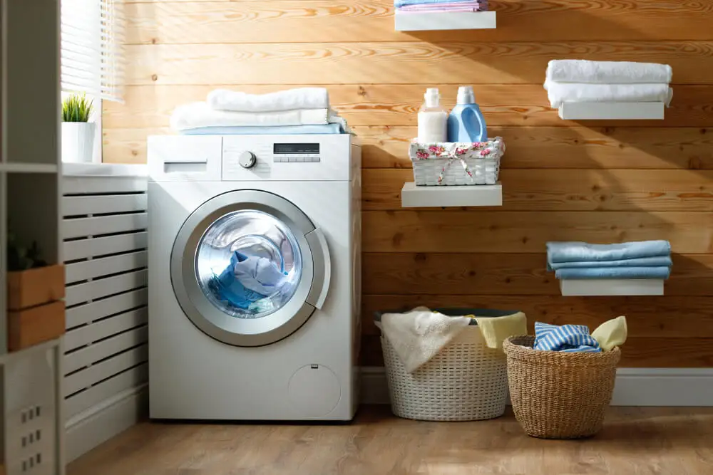 Modern laundry room with a front-load washing machine, wooden walls, shelves with towels, and laundry baskets