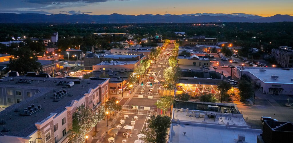 Aerial view of downtown Littleton, Colorado at dusk with glowing streetlights and distant mountain backdrop