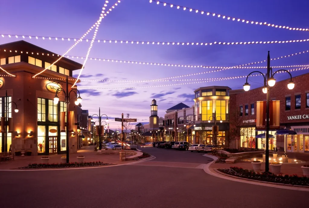 A vibrant shopping district at dusk illuminated by streetlights and overhead string lights.