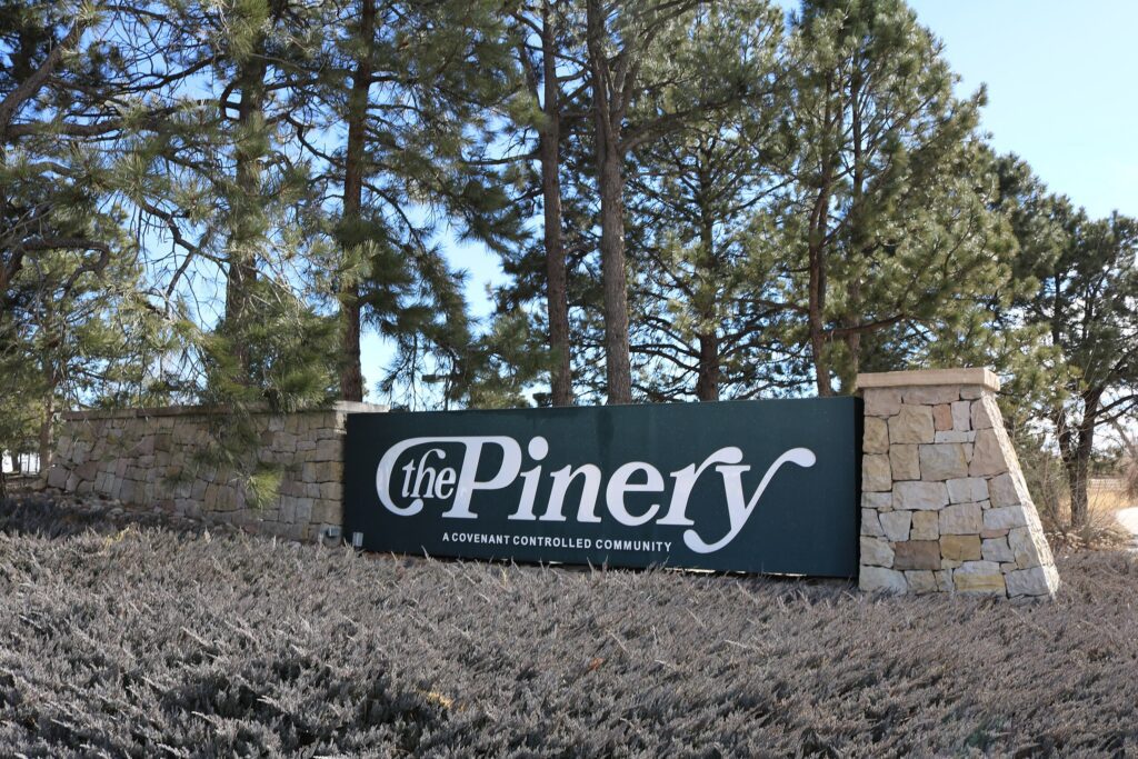 Entrance sign for The Pinery community surrounded by trees and stone pillars in Colorado