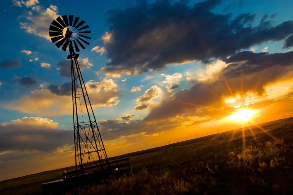 A windmill silhouetted against a vibrant sunset in Watkins, Colorado with a dramatic sky